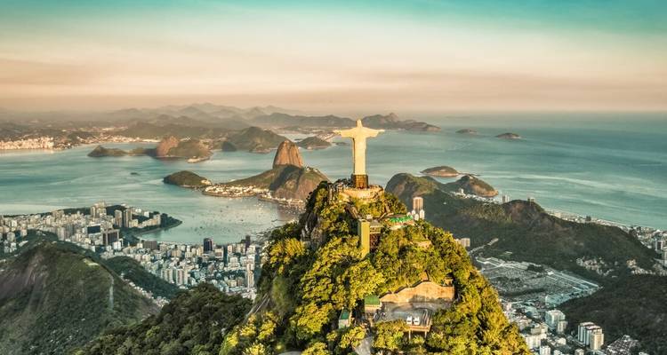 Aerial panorama of Rio de Janeiro with Christ the Redeemer atop lush mountain overlooking Guanabara Bay and Sugarloaf.