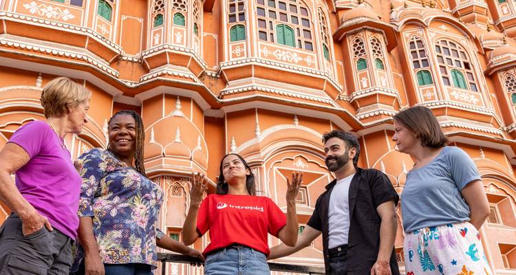 Een kleine toergroep praat druk met elkaar buiten de sierlijke roze gevel van Jaipur's Hawa Mahal.
