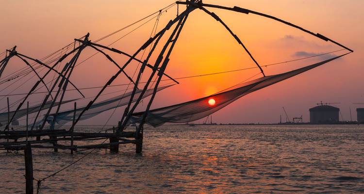 Silhouet van traditionele Chinese visnetten tegen een levendige oranje zonsondergang boven de Arabische Zee.