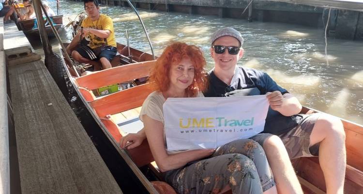 Couple souriant assis dans un bateau à longue queue en bois sur un canal tenant une bannière de l'entreprise avec des éclaboussures d'eau à proximité.