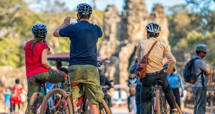 Les cyclistes portant des casques font une pause avec leurs appareils photo devant les anciennes portes en pierre d'Angkor.