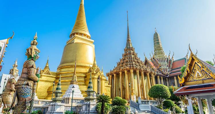 Grand Palace complex in Bangkok featuring the golden stupa and richly decorated temple buildings under a brilliant sky.