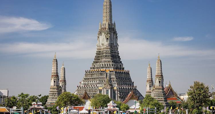 Full frontal view of the ornate Wat Arun temple with its central prang and surrounding smaller towers against a clear blue sky.