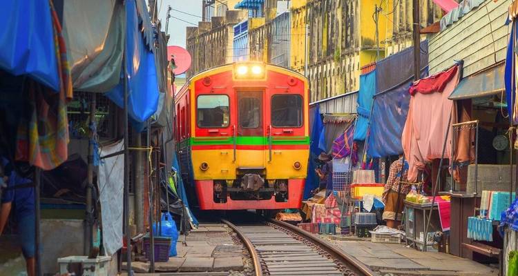 A bright yellow and red train squeezes through the narrow Maeklong Railway Market lined with colourful stalls.
