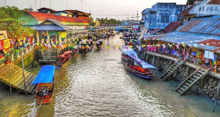 Lively canal scene of a Thai floating market with long-tail boats, colourful bunting and shops lining the waterway.