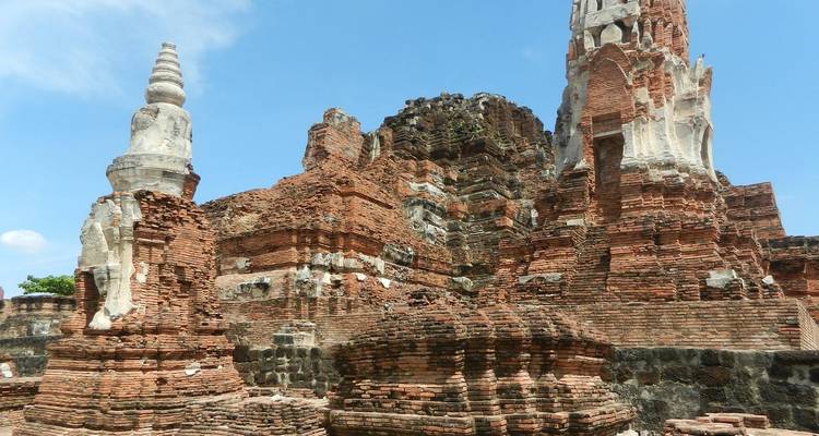 Ancient brick stupas and crumbling prangs of the Ayutthaya Historical Park under a clear blue sky.