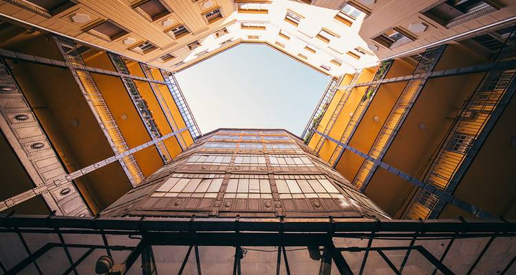 Looking straight up inside a light-filled courtyard surrounded by orange and cream balconies.