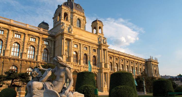 Vienna’s Kunsthistorisches Museum glows in warm evening light beside manicured hedges and statues.