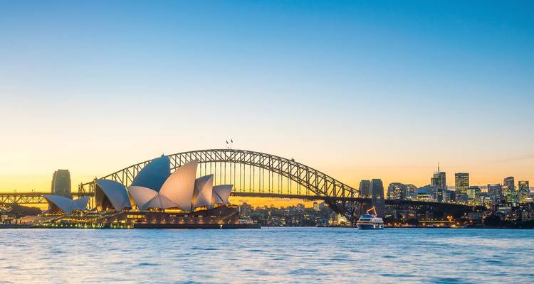 La Ópera de Sídney y el Puente del Puerto recortados contra un cielo dorado al atardecer con el skyline de la ciudad de fondo.