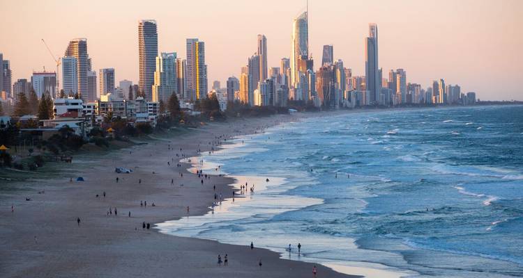 Horizonte de rascacielos de la Gold Coast bordeando una playa expansiva con una suave luz vespertina.