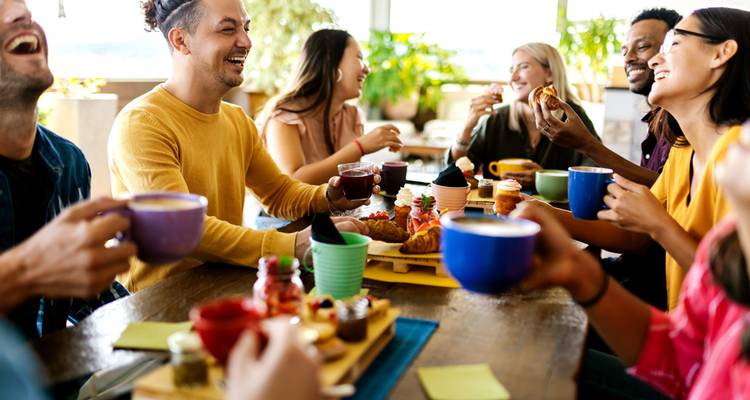 Amigos comparten café y pasteles riéndose alrededor de una mesa brillante en la cafetería.