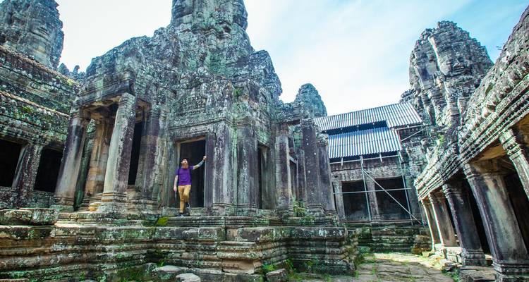 Der Reisende steht unter hohen Steinpfeilern und kunstvollen Schnitzereien des Bayon-Tempels innerhalb von Angkor Thom.