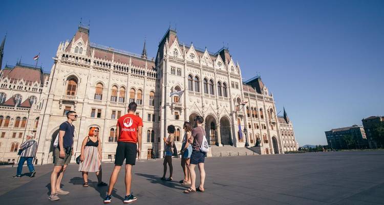 Travelers stand in front of the grand Hungarian Parliament under clear blue sky