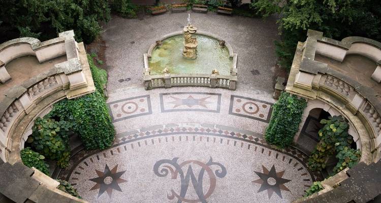 Symmetrical stone courtyard with fountain and ornate patterned mosaic viewed from above