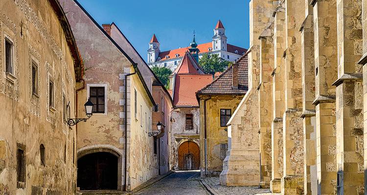 Cobblestone alley with historic facades leading to Bratislava Castle rising behind