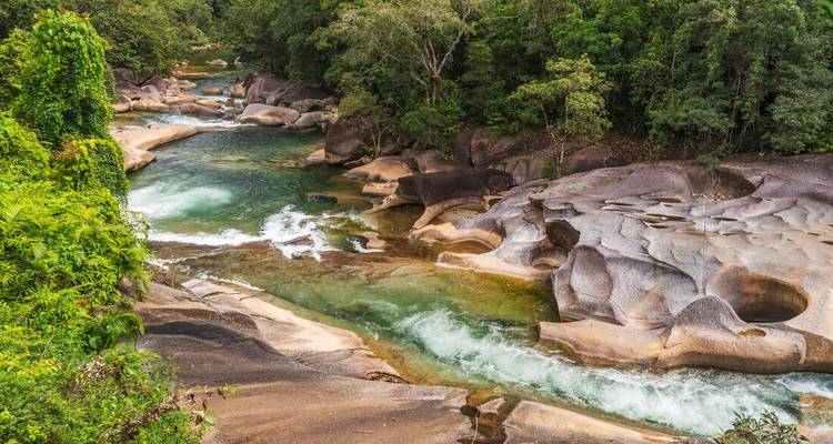 Clear green river flows through smooth sculpted granite boulders in tropical rainforest