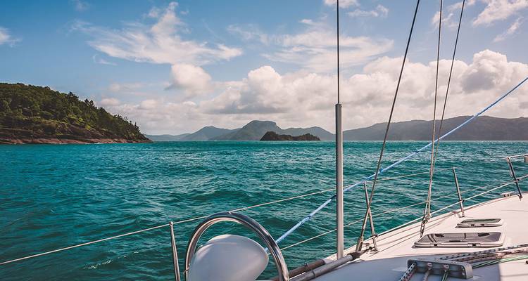 Sailboat deck points toward lush islands under bright clouds in Whitsundays