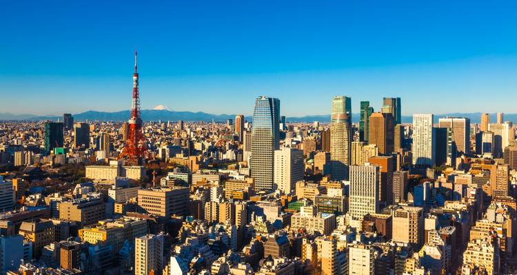Vue matinale dégagée de l'horizon de Tokyo mettant en vedette la Tour de Tokyo emblématique de couleur rouge et le Mont Fuji au lointain sous un ciel bleu.