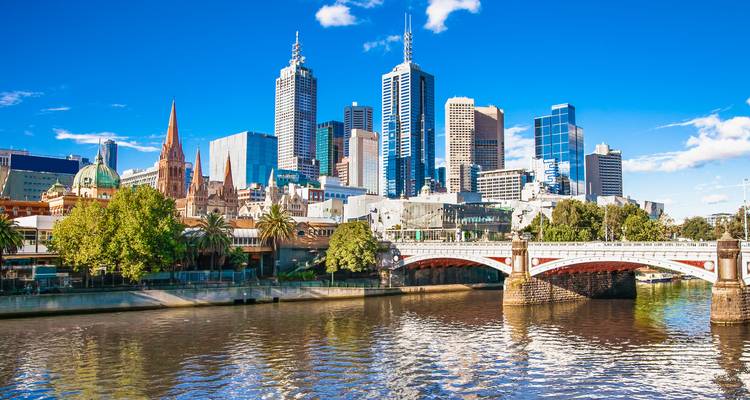 Vista diurna brillante de los rascacielos del CBD de Melbourne reflejados en el río Yarra con el puente de arco en primer plano.