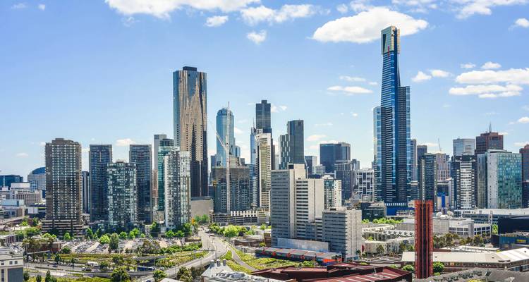 Panorama moderno de rascacielos de Melbourne con la Torre Eureka destacándose contra un cielo azul con nubes dispersas.
