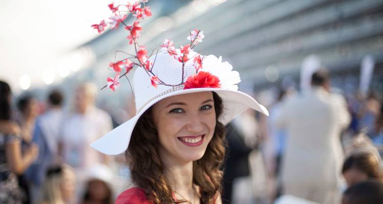 Mujer sonriente usando un elaborado tocado floral en un evento al aire libre concurrido, con un fondo suavemente desenfocado.