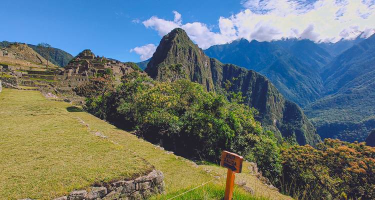 Alternate angle of Machu Picchu with foreground greenery and wayfinding sign.