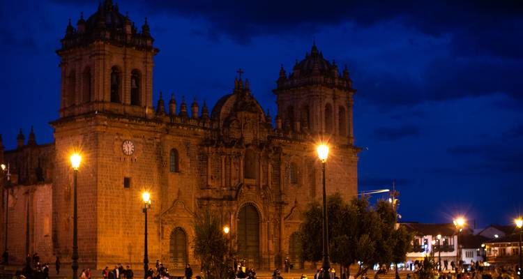 Vue nocturne de la Cathédrale de Cusco illuminée par les réverbères contre un ciel bleu profond.
