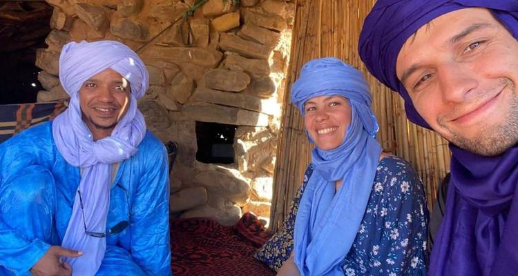 Trois amis souriants portant des turbans bleus à l'intérieur d'une hutte en pierre rustique
