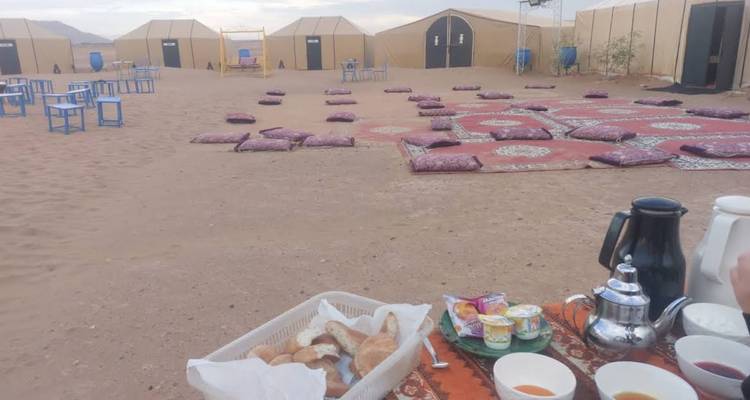 Configuration du petit-déjeuner matinal avec du pain et des coussins dans un campement désertique de sable avec des tentes en toile.