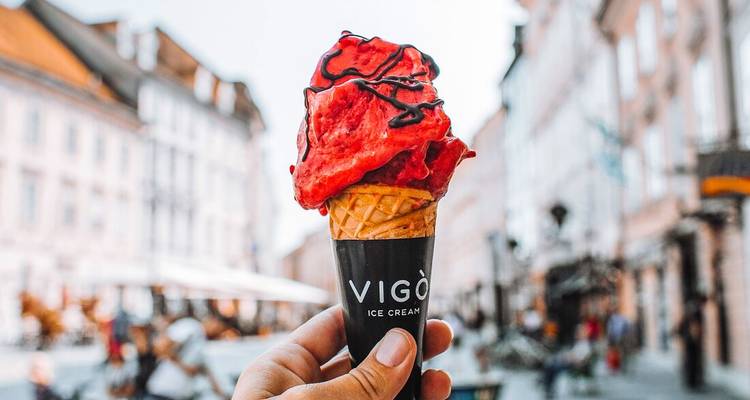 A vibrant red gelato cone from VIGO Ice Cream held up against a charming European street.