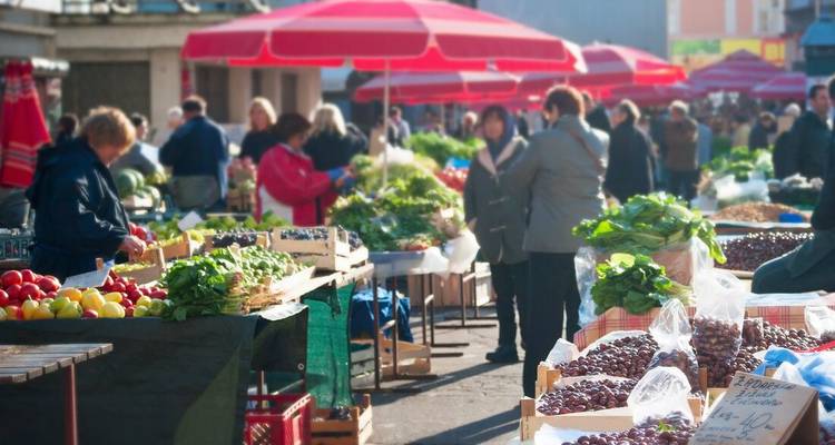 Bustling outdoor market with red umbrellas, fresh produce and shoppers.