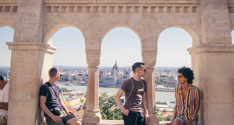 Three friends sit in arches of Fisherman’s Bastion overlooking the Danube and Parliament
