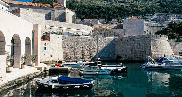Small boats moored in a historic stone harbour enclosed by fortified city walls