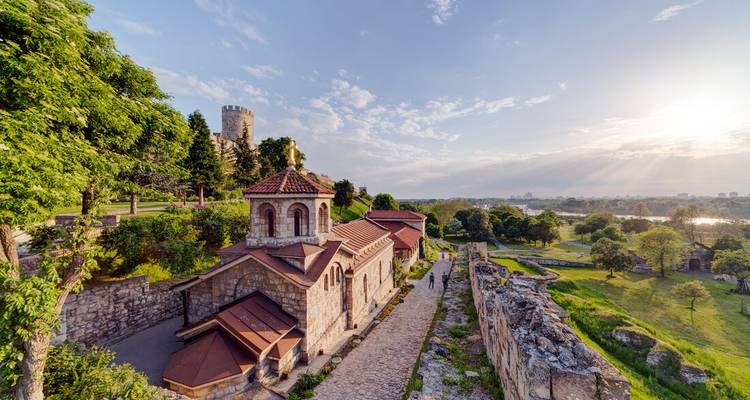 Stone church and fortress tower on a green hilltop overlooking a riverside park at golden hour
