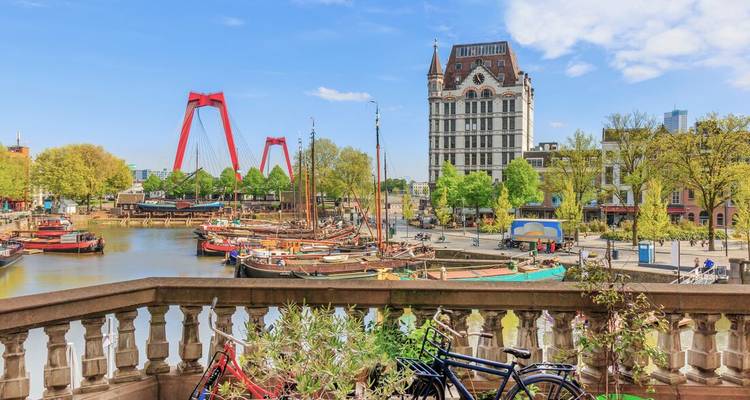 Historic harbour with vintage boats, red suspension bridge and ornate white tower under blue sky