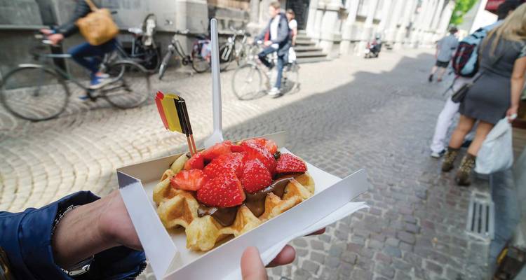 Belgian waffle topped with strawberries and chocolate sauce being held on a cobblestone street