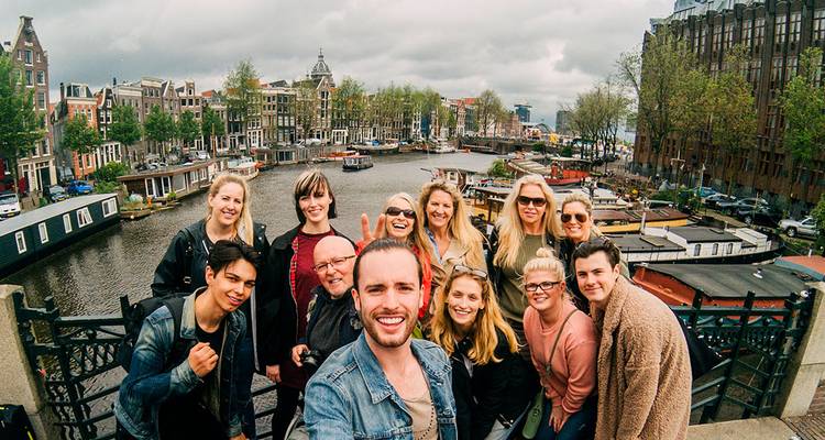 Smiling travellers taking a selfie on a bridge overlooking houseboats and canals on a cloudy day