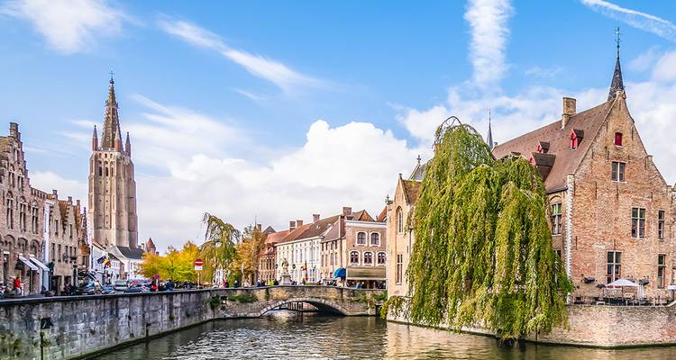 Picturesque canal with stone bridge and tall church tower rising above medieval buildings