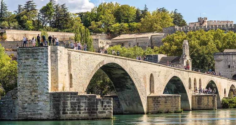 Pont de pierre médiéval enjambant une rivière avec des foules se promenant le long, en arrière-plan des murs fortifiés