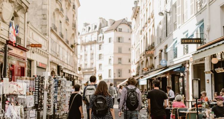 Vue arrière de voyageurs se promenant dans une rue parisienne animée bordée de boutiques et de cafés