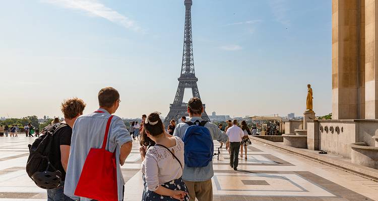 Les touristes se rassemblent sur une place face à la Tour Eiffel par une belle journée, prenant des photos et admirant la vue.