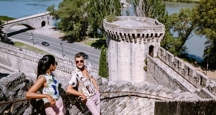 Un couple élégant s'arrête sur de vieilles marches en pierre dominant le pont médiéval d'Avignon et les remparts de la ville à côté du Rhône.