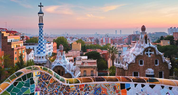 Le banc en mosaïque colorée et les toits fantaisistes du Park Güell encadrent une vue à l'aube sur Barcelone.