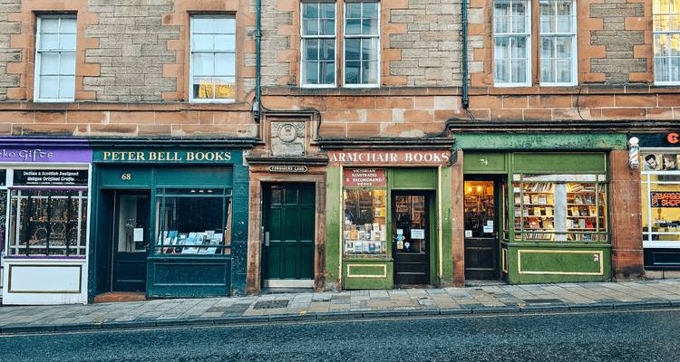Colorful storefronts of small independent bookshops along a quiet stone street in an old Scottish town.