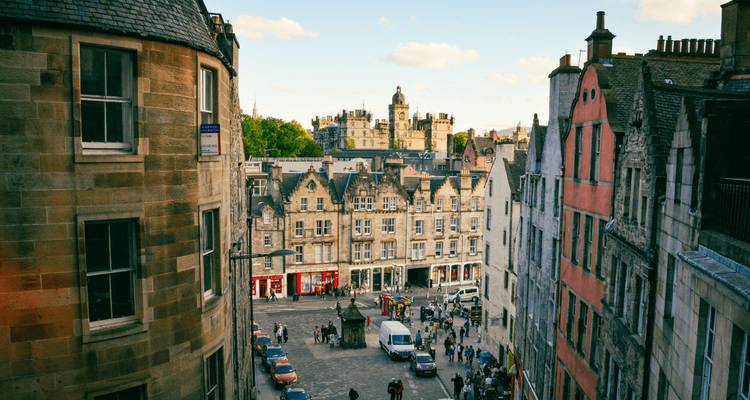 Elevated view of a historic stone street lined with tall townhouses leading toward Edinburgh Castle under a clear sky.