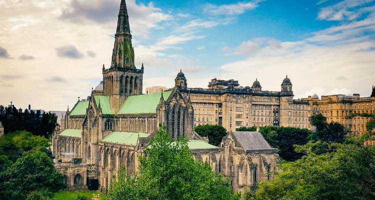 Neo-Gothic cathedral with green copper roofs rising above treetops in a cityscape under a partly cloudy sky.