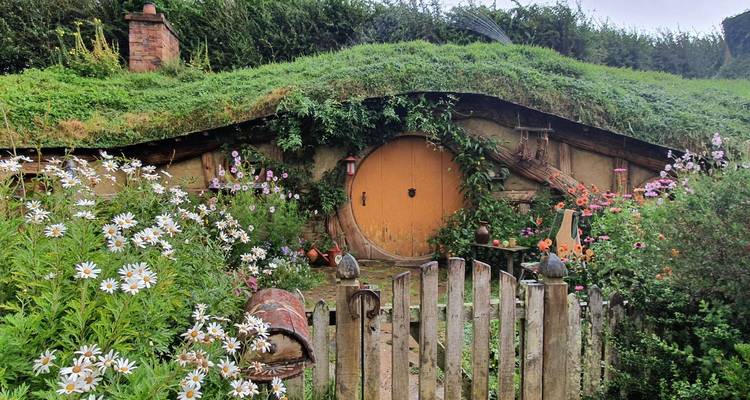 Charming hobbit hole with round yellow door surrounded by flowering garden.