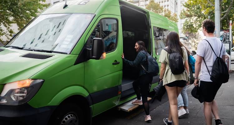 Travellers step into a bright green shuttle van on a city street.