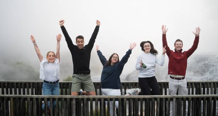 Young travellers jump joyfully on a boardwalk amid geothermal steam.