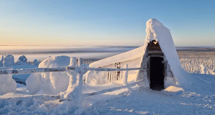 Cabane et clôture enneigées au sommet d'une montagne dominant un vaste désert gelé au lever du soleil.